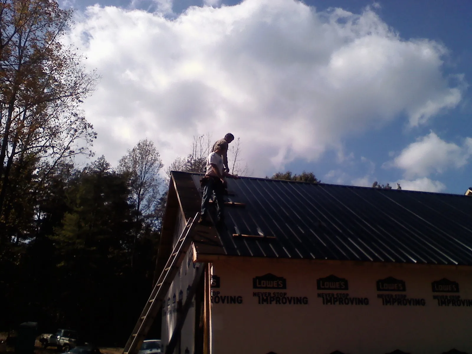 Roofer fastening dark metal panels high against a cloudy sky, from a Roof Inspection job in Ringgold